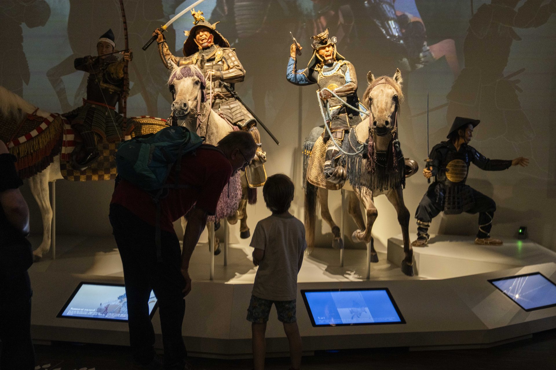 Ein Mann und ein Kind stehen vor einer Vitrine mit 4 Samurai Figuren mit Pferden im Samurai Museum