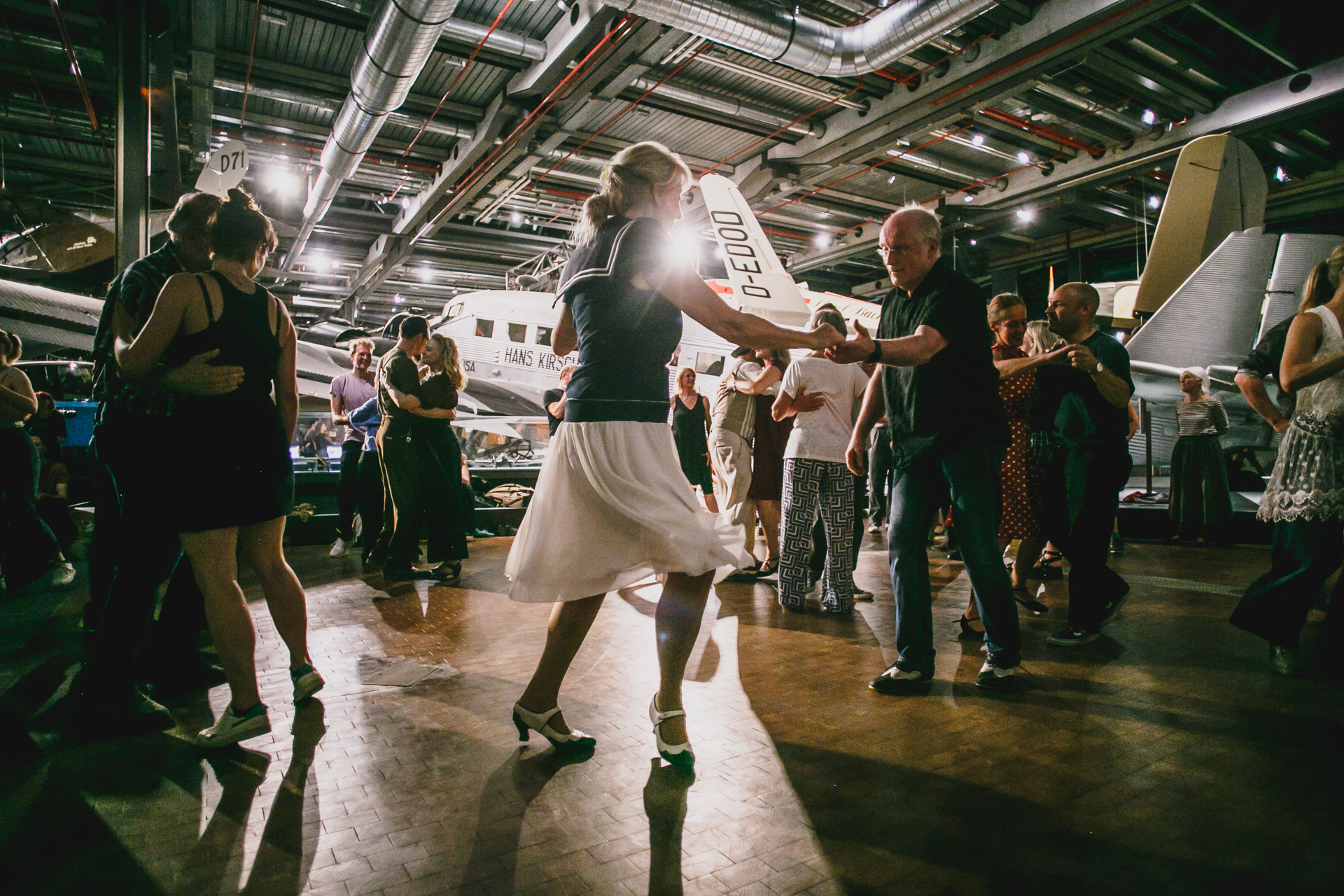 Dancing people in a hall with airplanes, vibrant atmosphere at a dance event.