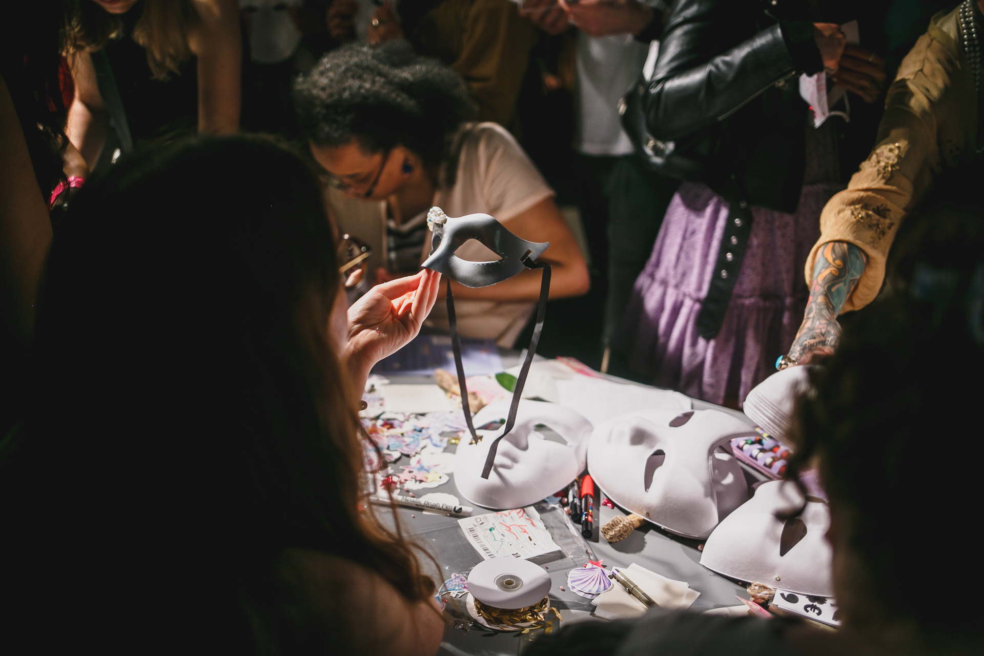 People are making masks at a table, surrounded by craft materials in a creative atmosphere.