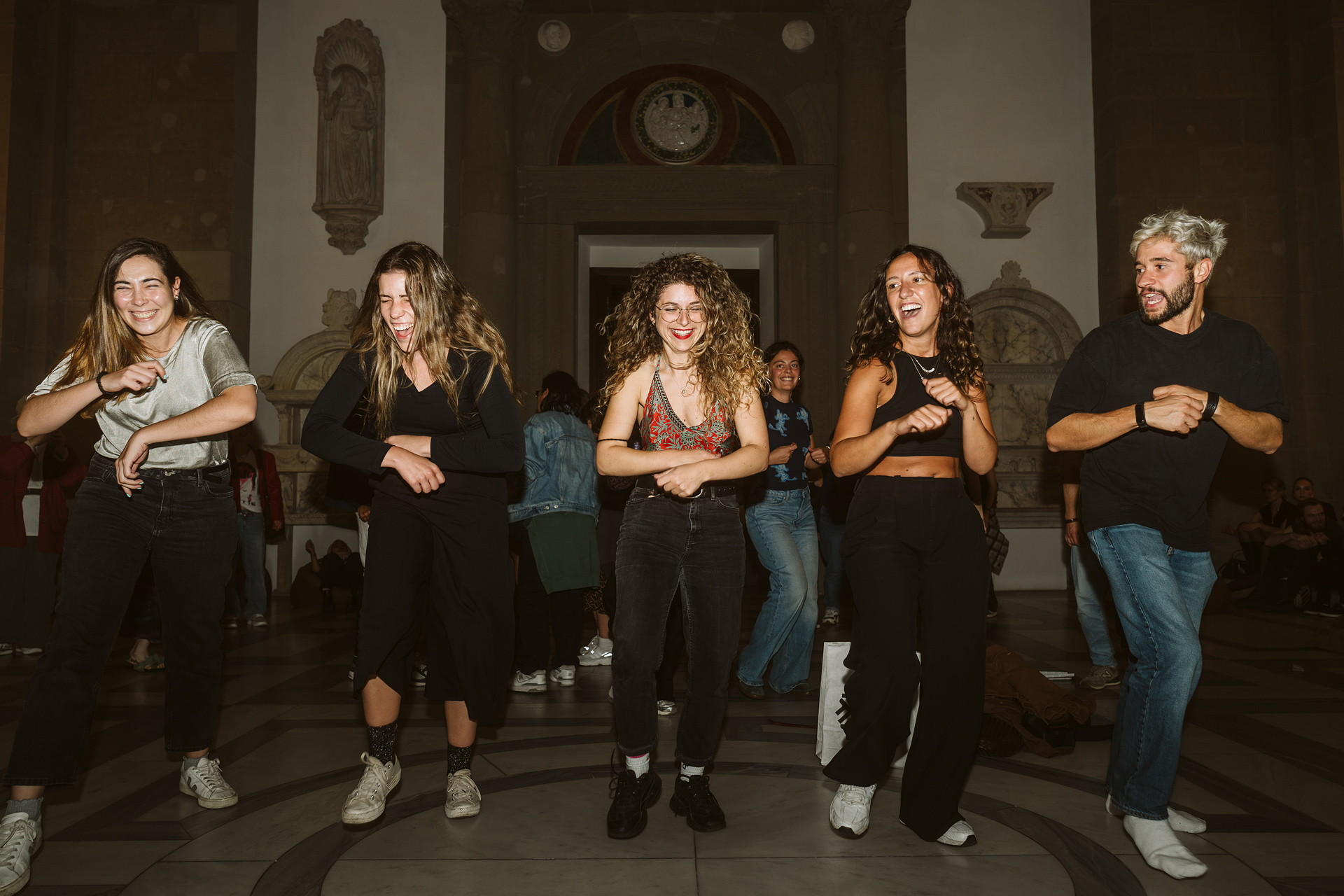 Five people are happily dancing in a room with a historic ambiance. Fun and joy are evident.