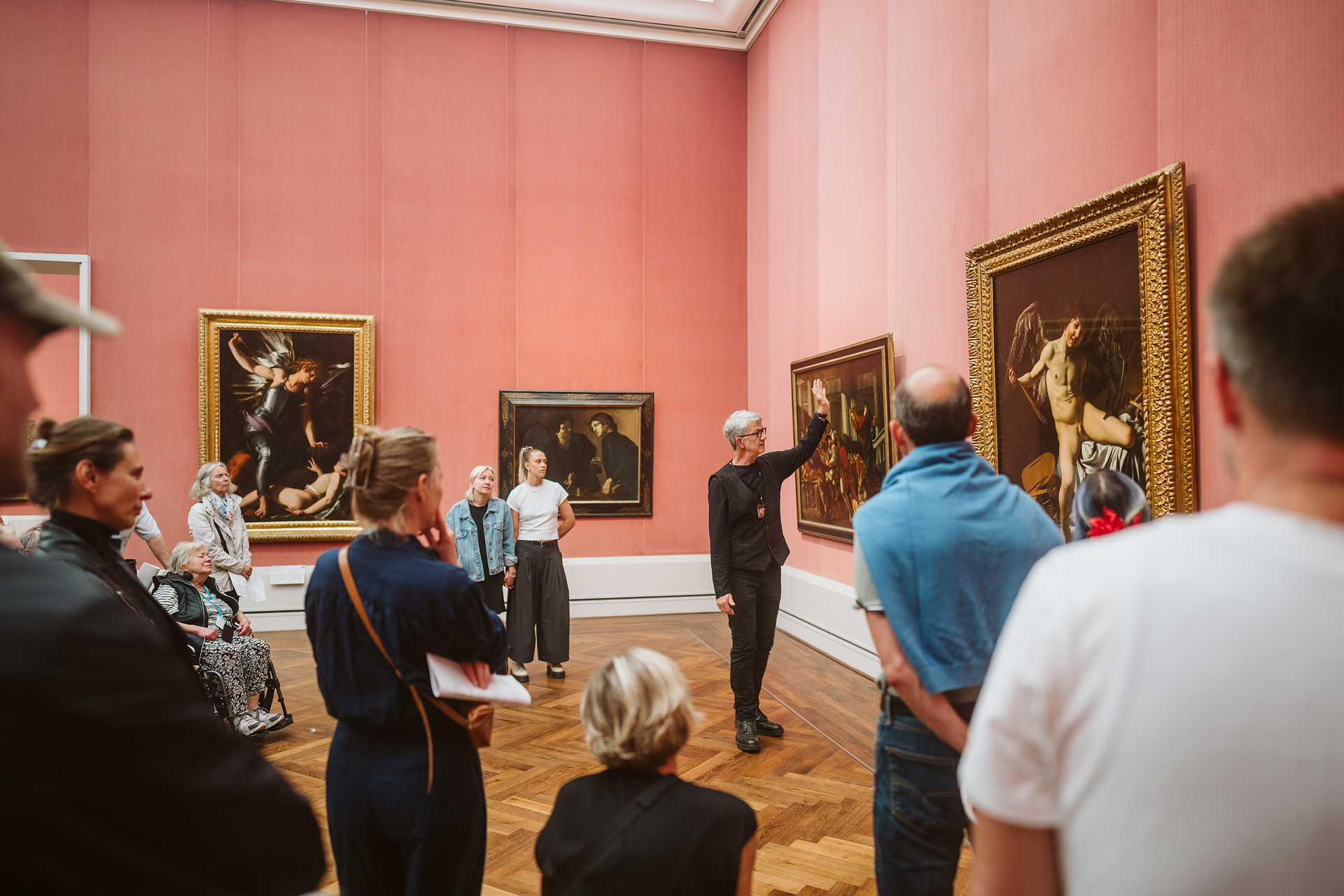 Tours of an art gallery with a group of visitors and a curator explaining artworks.