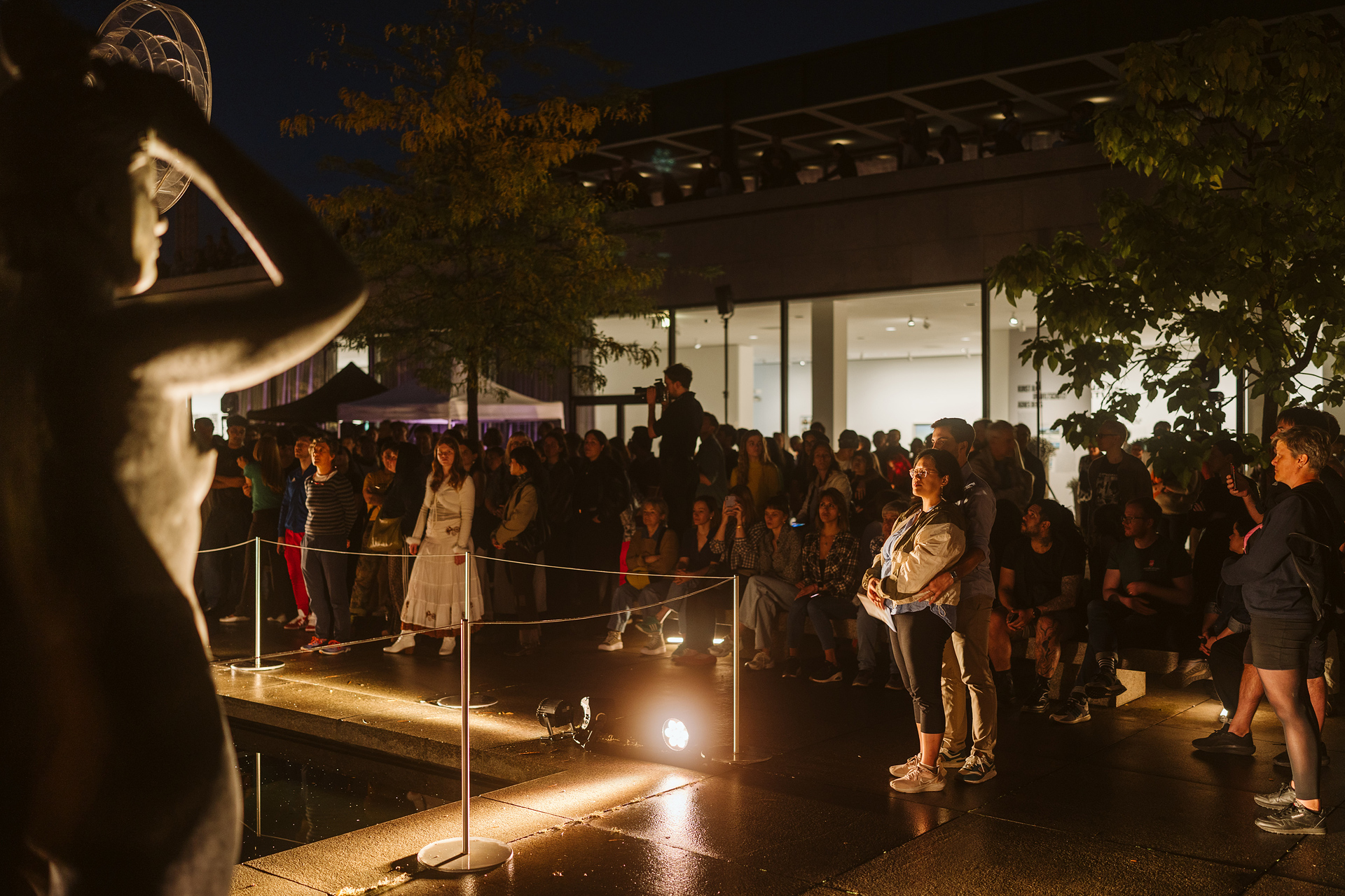 A crowd admires a statue at night, surrounded by lights and a modern art ambiance.