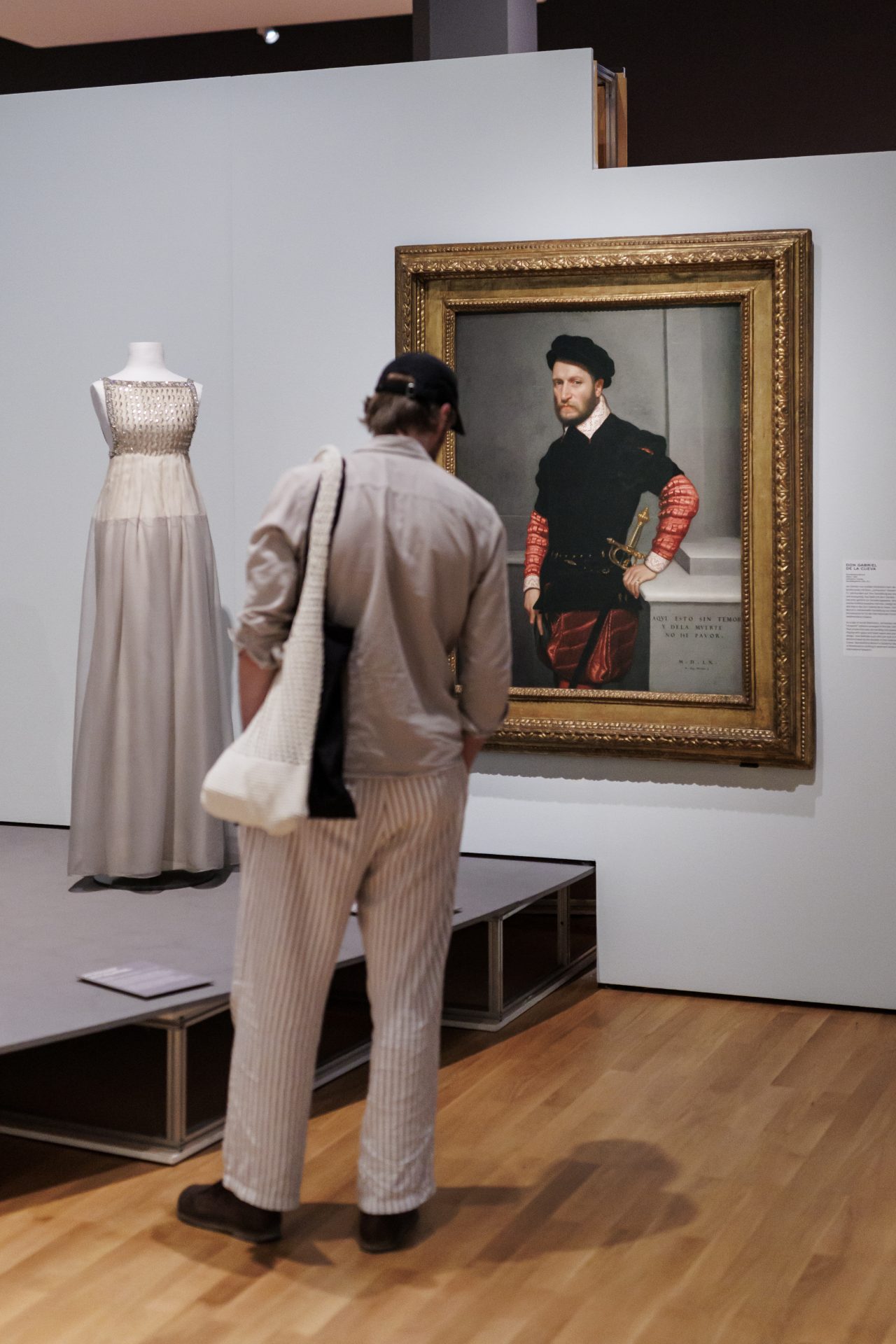 Besucher betrachtet ein Gemälde und ein Kleid in einem Museum. Im Hintergrund ist eine elegante Skulptur sichtbar.