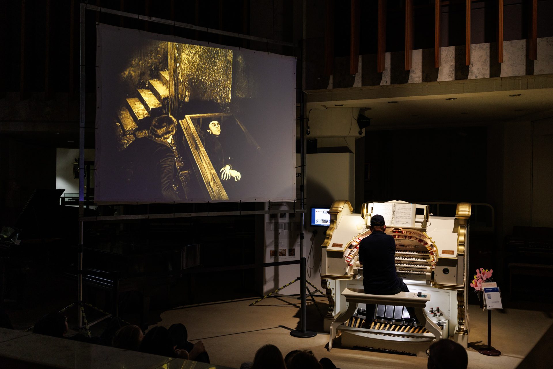 Stummfilmvorführung mit Live-Orgelmusik; Musiker spielt vor einer Leinwand mit einer Filmszene aus einem klassischen Horrorfilm.